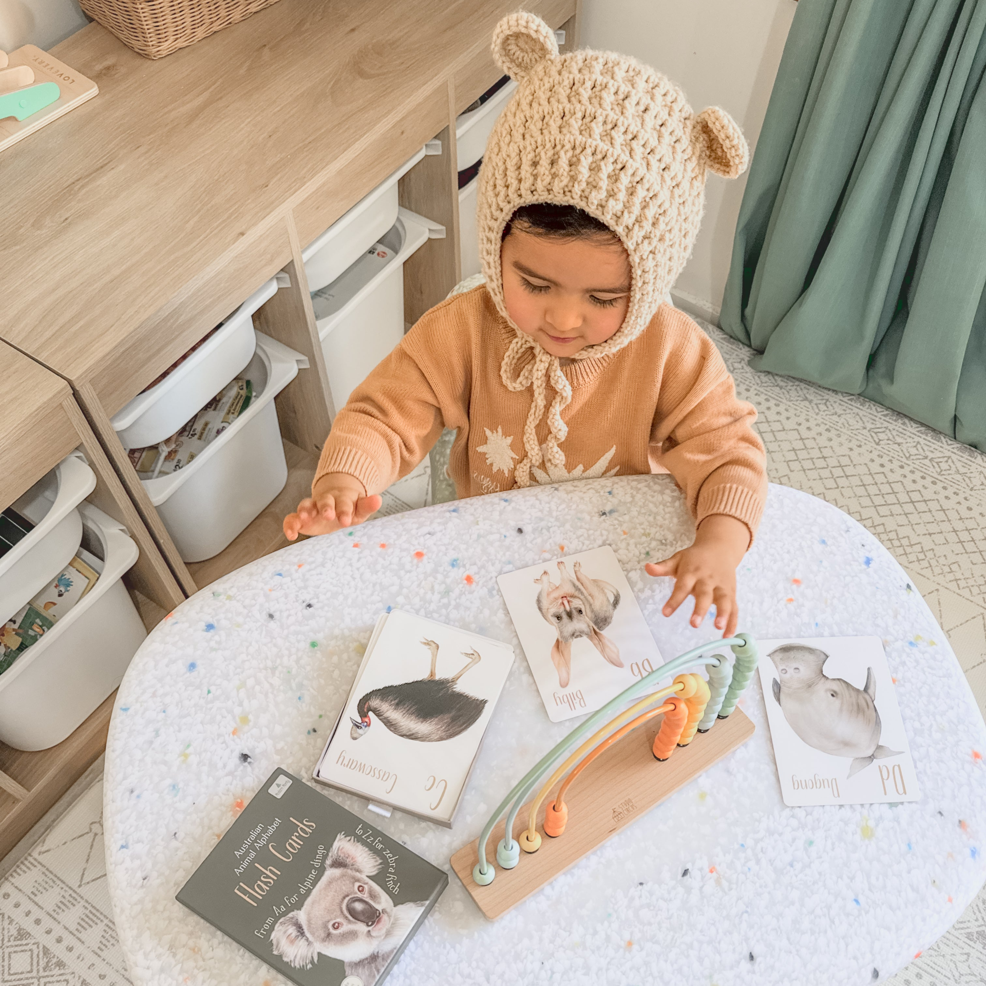 White confetti table with books with australian animals and a little girl wearing a knitted bear ears beanie