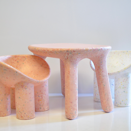 pink table and pink and white roly poly chair with a speckled confetti pattern on a white surface and background