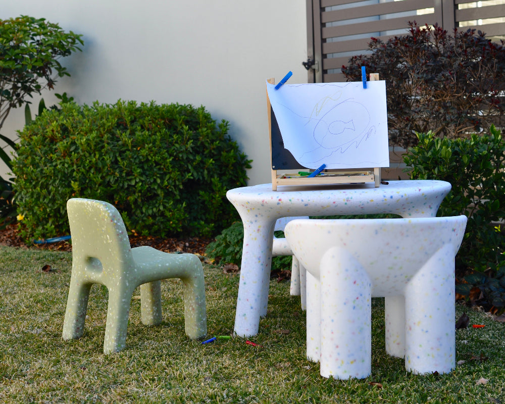 Children's outdoor art station with an easel, table, and chairs on grass.