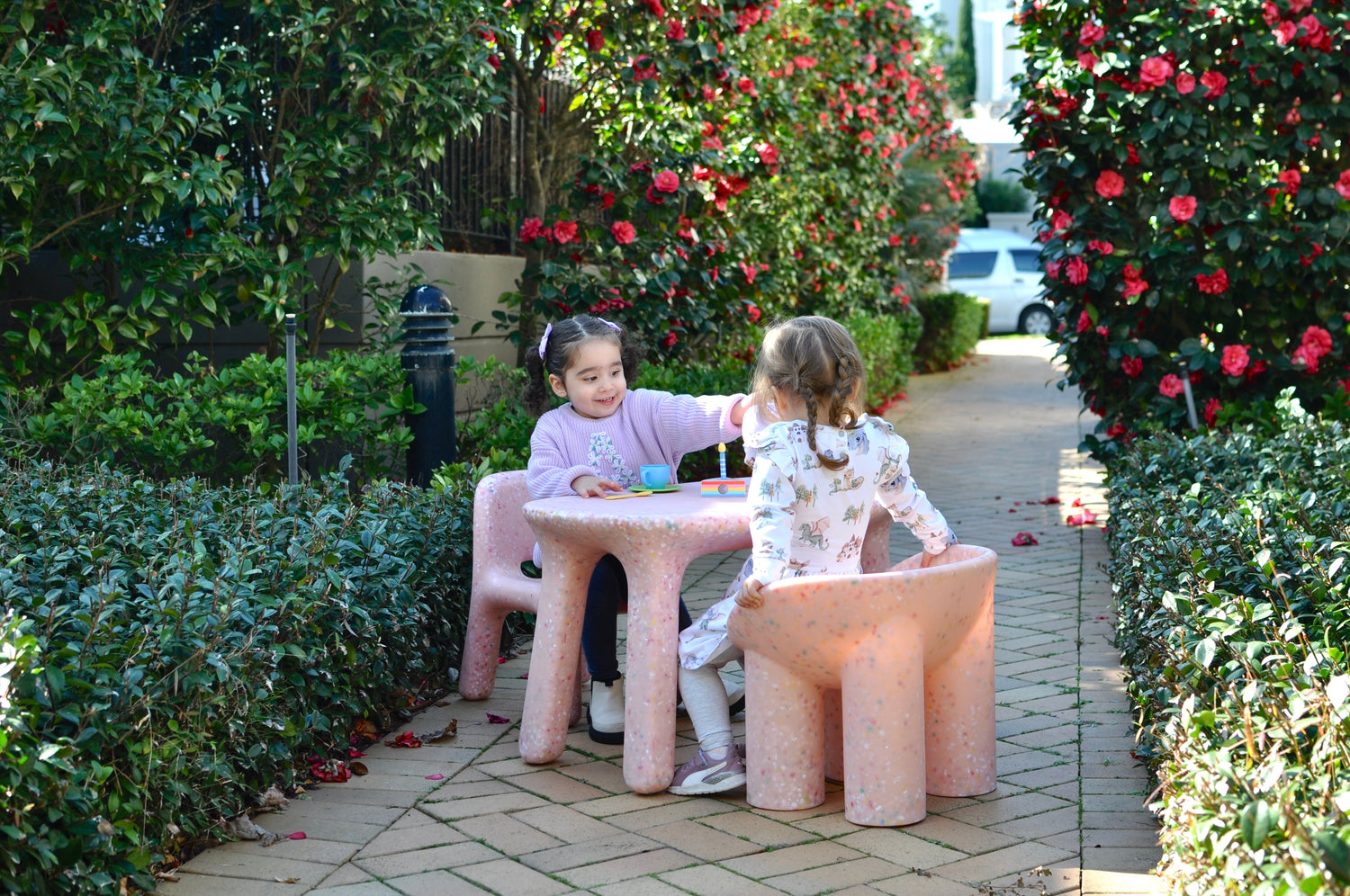 two little girls sitting in the garden playing high tea on a kids pink speckles confetti table and chair set 