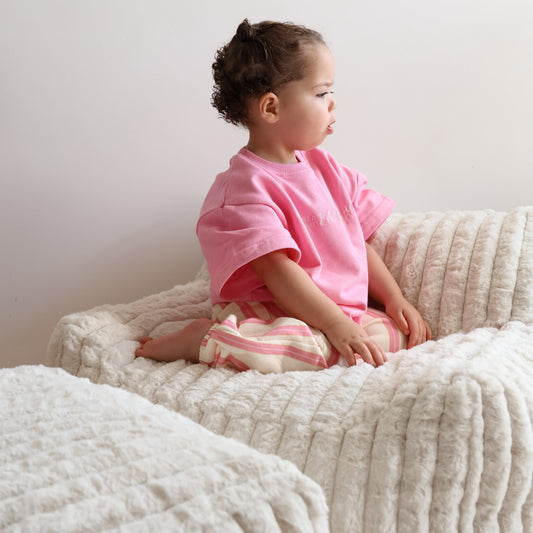 Child in a pink shirt sitting on a textured kids couch mini lounger chair against a white wall