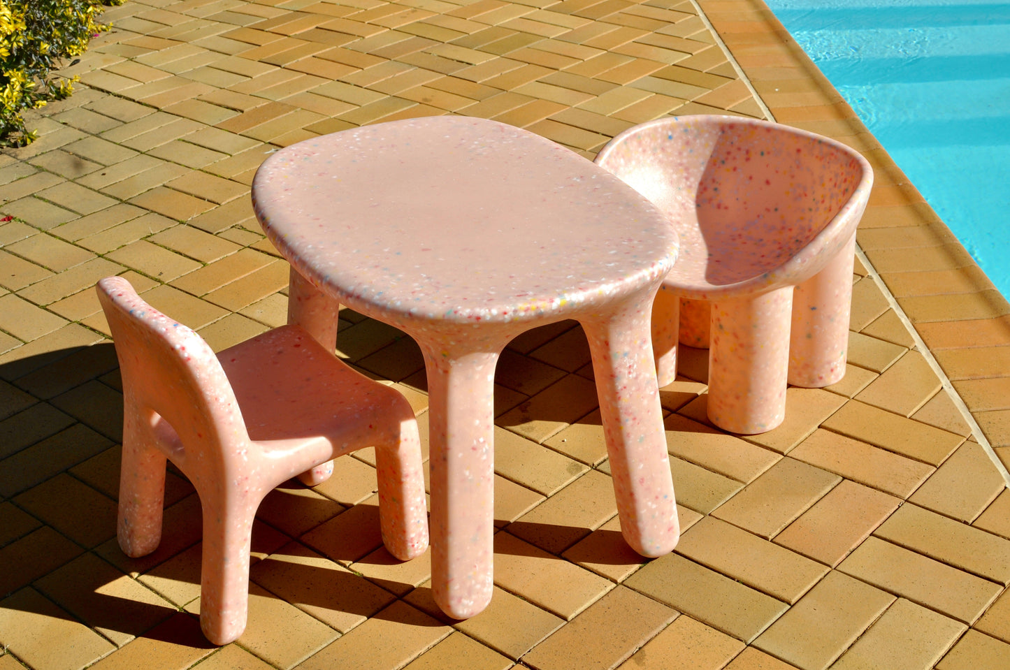 Set of two pink children's chairs and table on a tiled patio by a pool