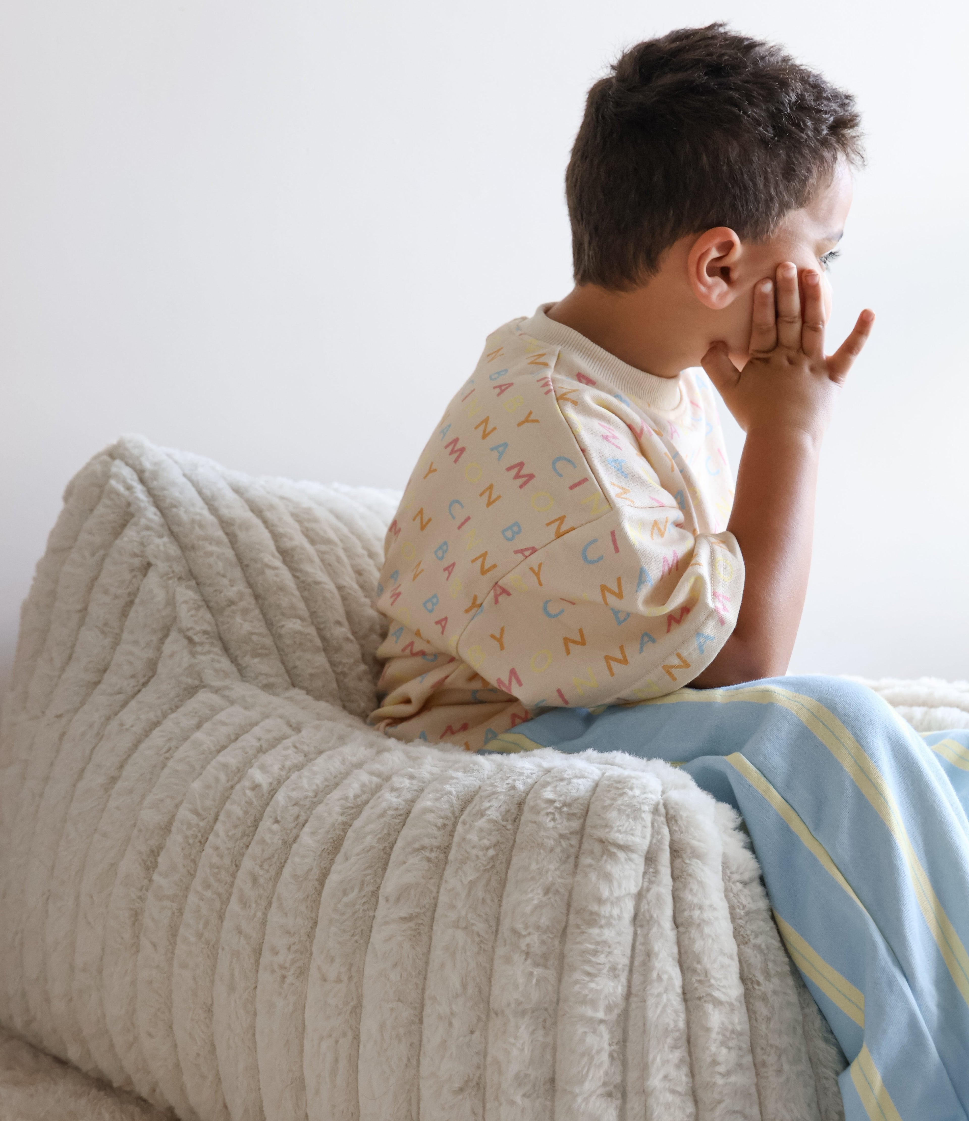 Child in pajamas sitting on a speckles kids' couch mini lounger, looking thoughtful.