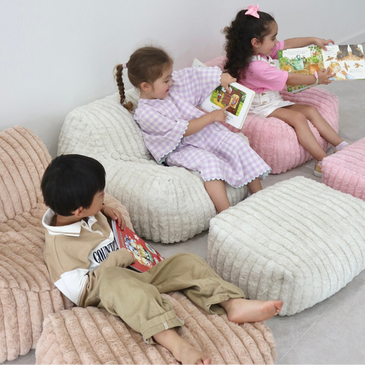 Children sitting on textured bean bags and ottomans reading books in a cozy room.