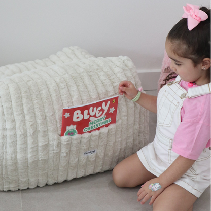 Child interacting with a large textured pillow featuring a 'Bluey' Christmas design book