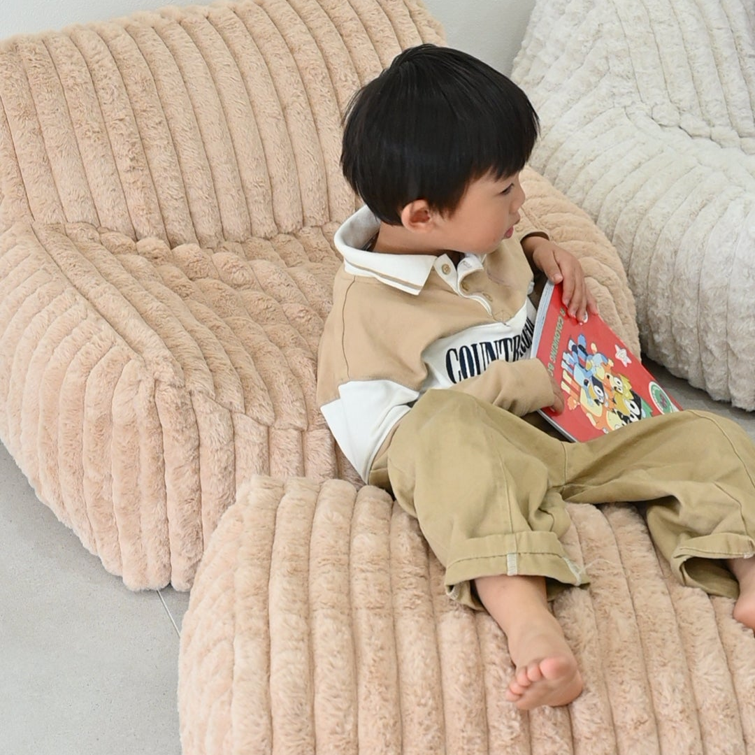 Child sitting on a textured beige speckles kids couch mini sofa reading a book