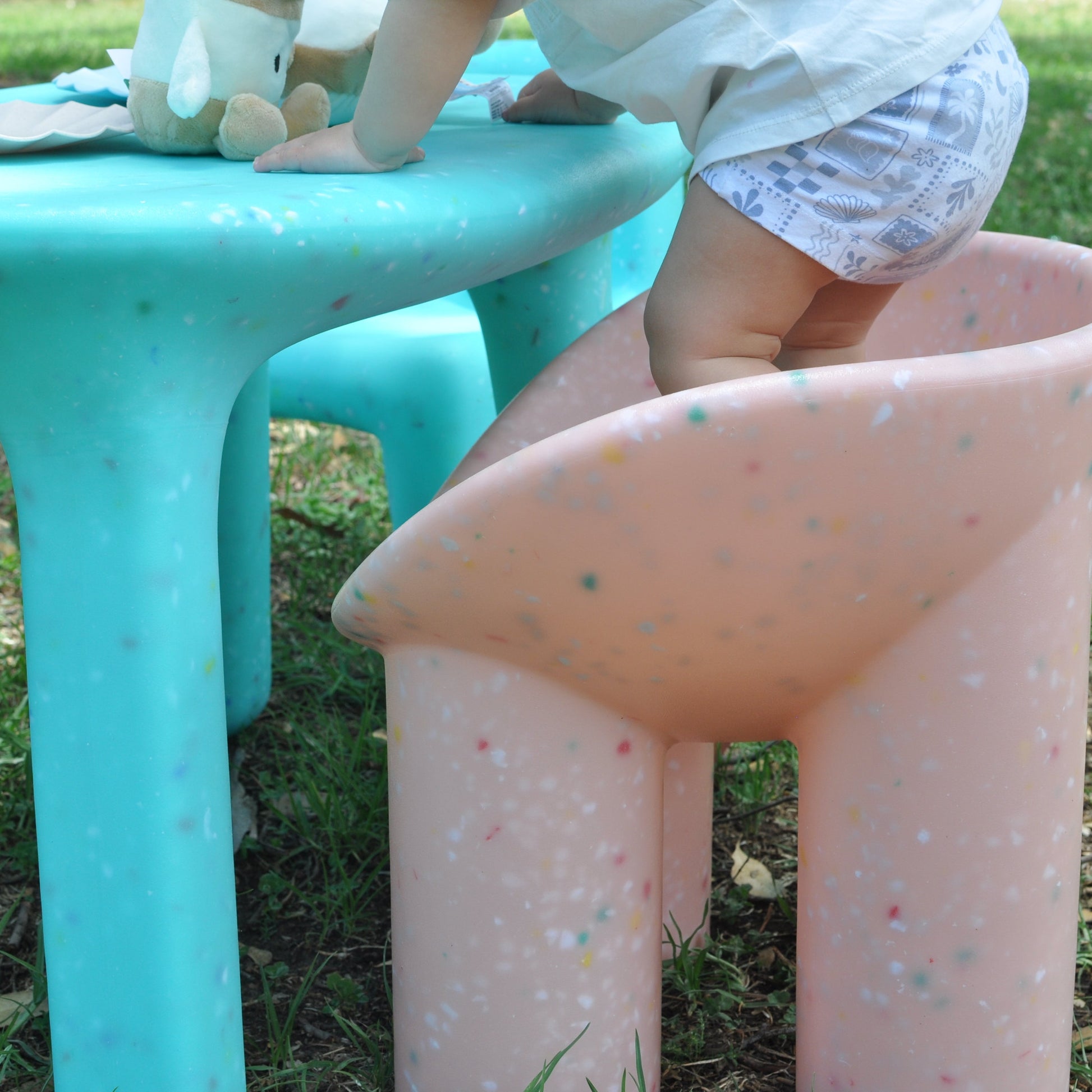 Child standing on a pink blossom confetti roly poly chair outdoors next to turquoise blue confetti table.