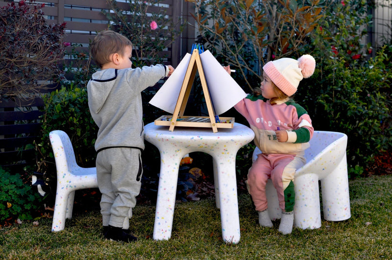girl and boy painting in the garden, sitting on white confetti tables and chairs set