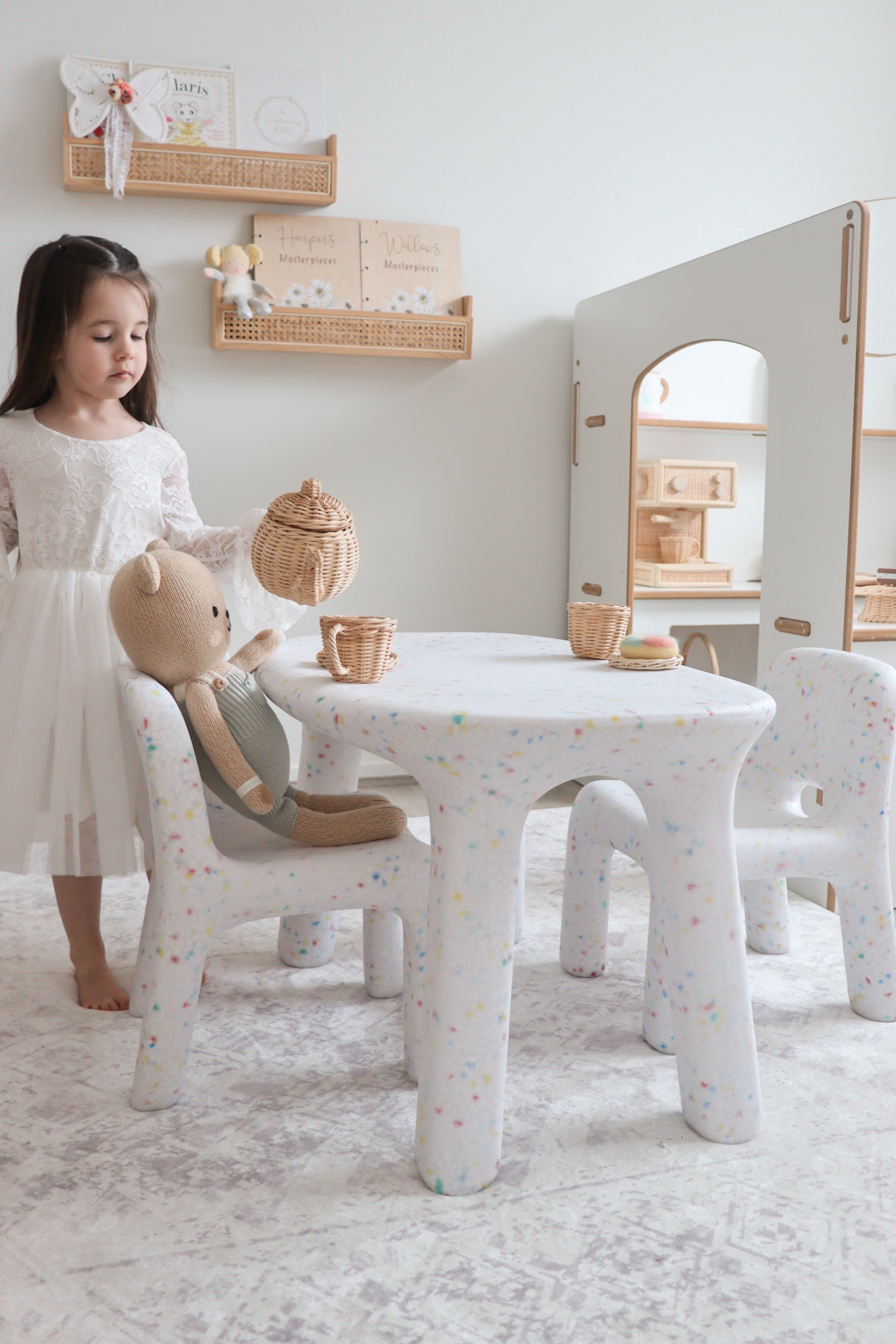 Child playing with toys at a small white speckled confetti table and chair set in a bright children's playroom. A photo shot to feature speckled children's furniture set